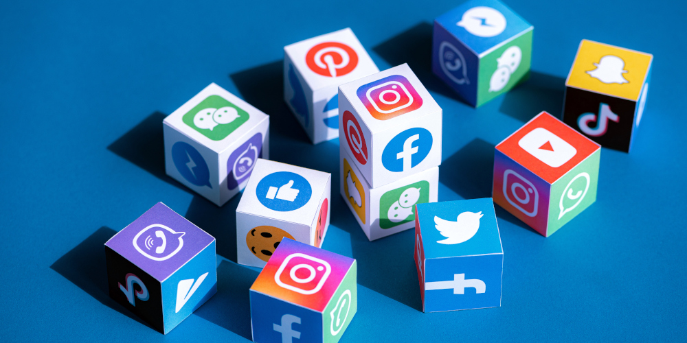 3D cubes displaying popular social media logos, including Facebook, Instagram, YouTube, Twitter, Snapchat, TikTok, and more, on a blue background.